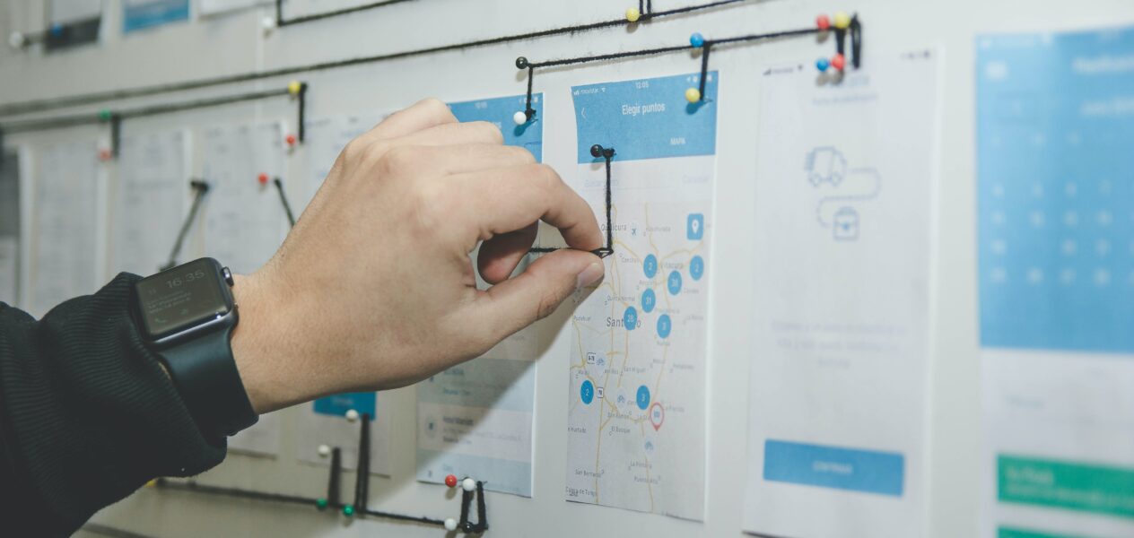 hand updating intricate storyboard of mobile mockups with yarn and push pins
