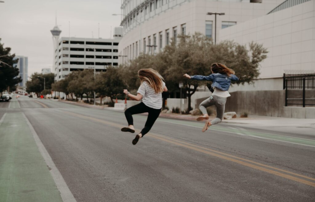 Two women jumping joyfully in an empty city street, highlighting the freedom of efficient production support with runbooks.