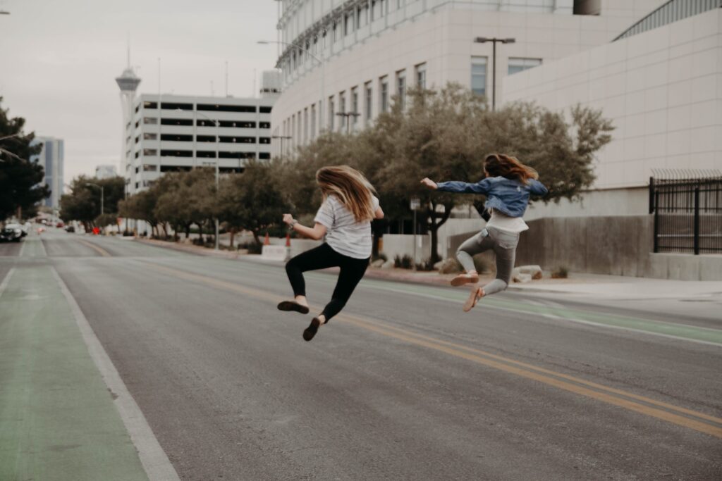 Two women jumping joyfully in an empty city street, highlighting the freedom of efficient production support with runbooks.